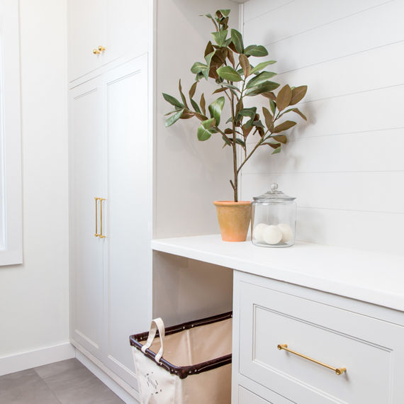 Laundry room with white subway tile on backsplash, white cabinets, and gold accents.