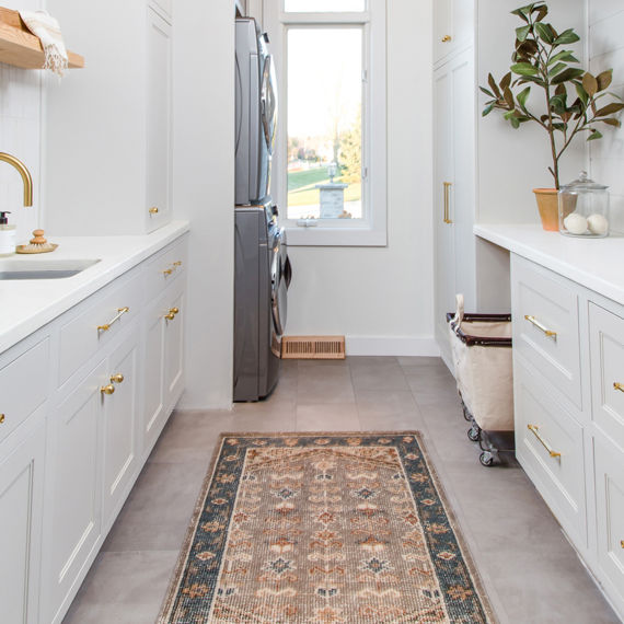 Laundry room with white subway tile on backsplash, white cabinets, and gold accents.