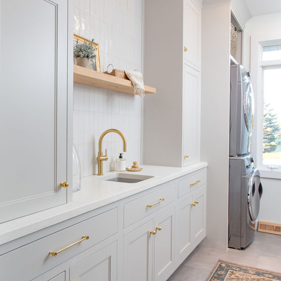 Laundry room with white subway tile on backsplash, white cabinets, and gold accents.