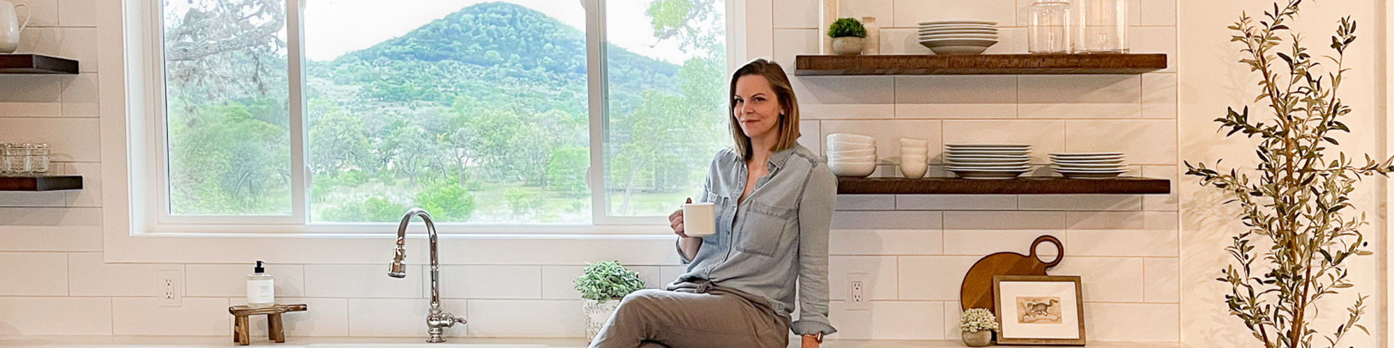 Jennifer Gizzi in her parents newly renovated kitchen with white subway tile backsplash, white quartz countertops, floating wood shelves, and gray lower cabinets.