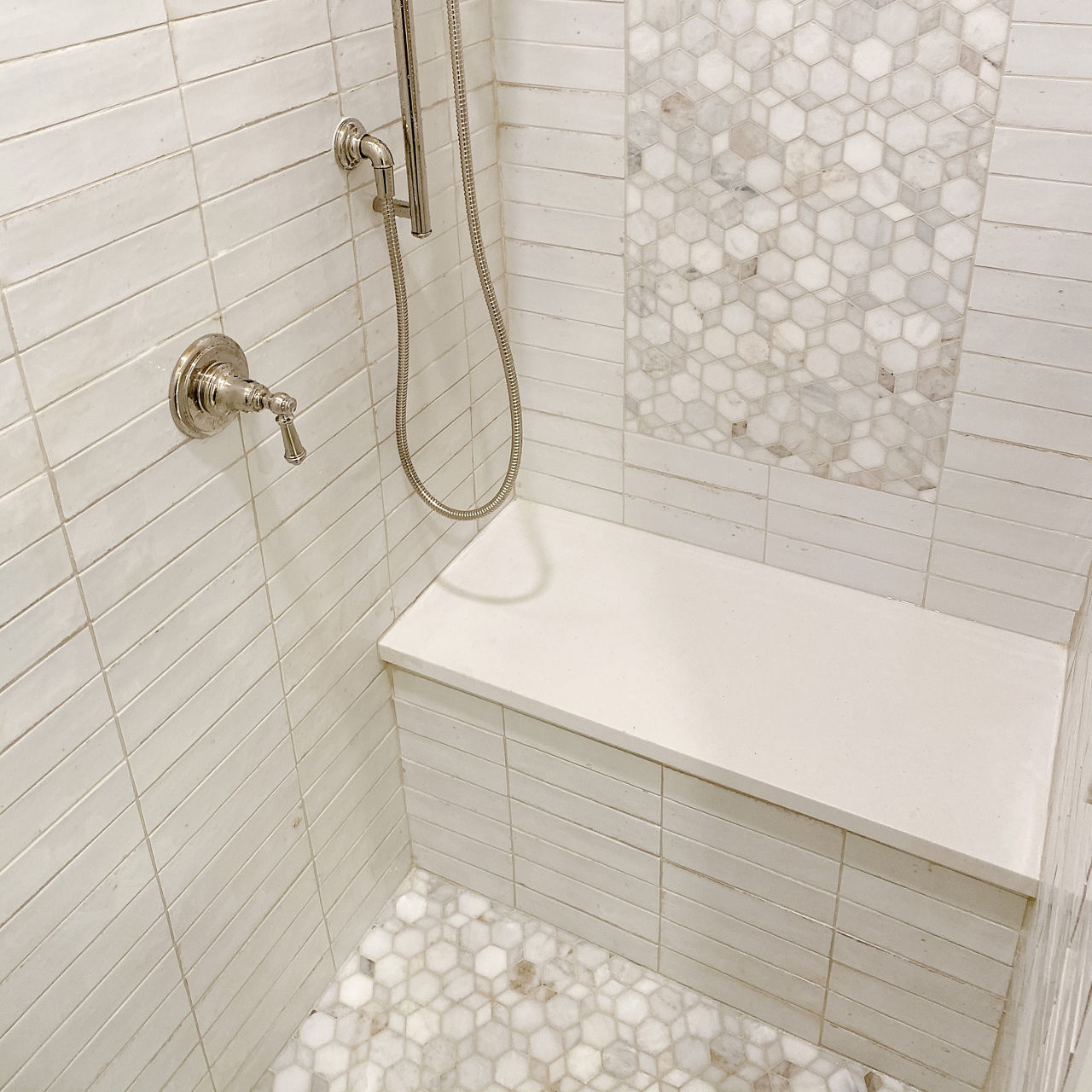 Recently renovated bathroom with white and beige marble mosaic shower floor and wall accent, white glossy shower wall tile, and brushed gold fixtures.