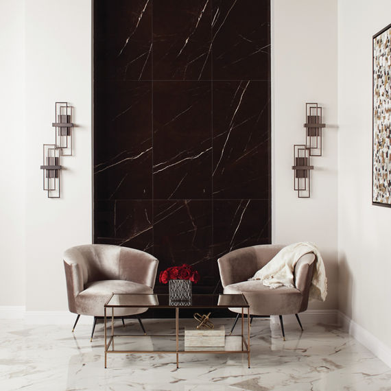 Sitting area with white marble look floor tile, black rectangle marble look tile on back wall, white walls, and two gray velvet sitting chairs.