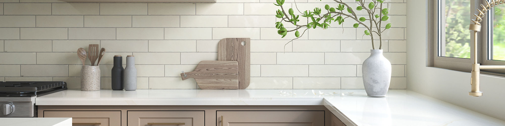 Kitchen with white subway tile on backsplash, white marble look porcelain countertop, light beige cabinets, and a white vase and wooden cutting boards on the counter.