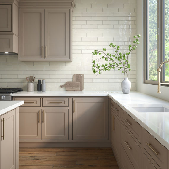 Kitchen with white subway tile on backsplash, white marble look porcelain countertop, light beige cabinets, and a white vase and wooden cutting boards on the counter.