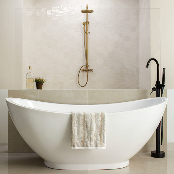 Bathroom with white hexagon tile on back wall, white curved bath tub, gold shower head, and white square floor tile.