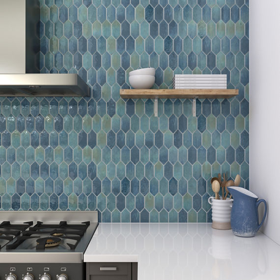 Kitchen close up of blue picket mosaic on backsplash, white countertop, and wooden shelf with dishes.