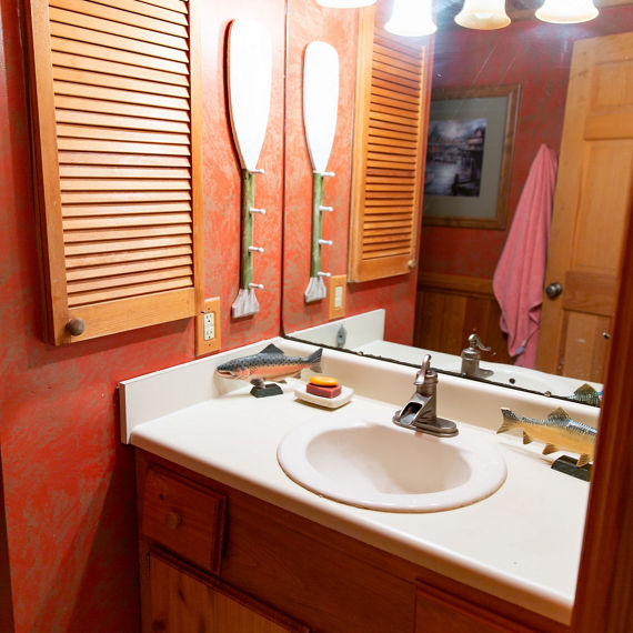 Before photo of bathroom with white countertop and sink, wall mirror, red wallpaper, natural wood medicine cabinet and vanity.