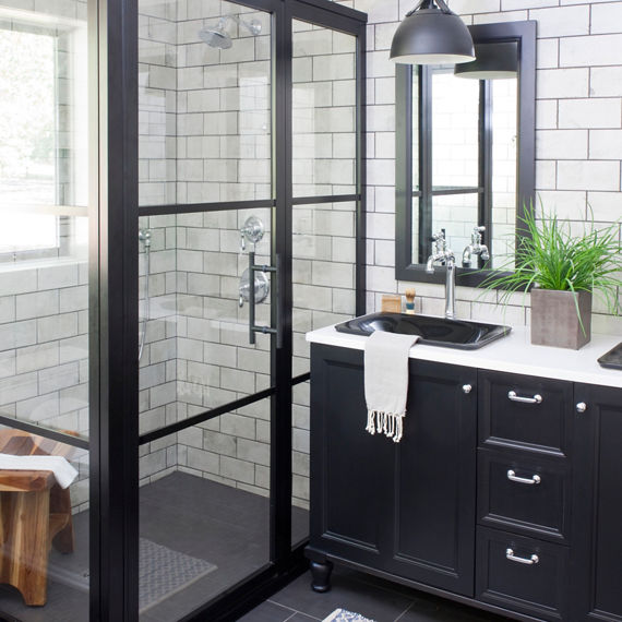 Bathroom with white stone look rectangle tile in a brick pattern on backsplash and inside shower, black hexagon mosaic tile on shower floor, and silver accents.