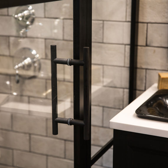 Close up of white stone look rectangle tile in a brick pattern inside shower walls and backsplash, and silver accents.