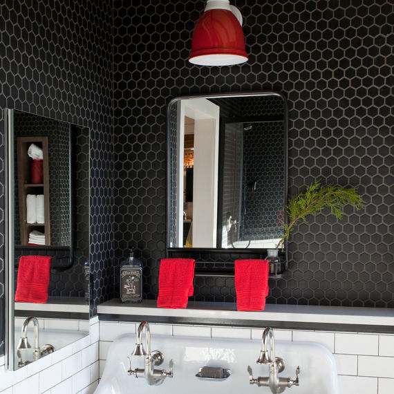 Bathroom sink with black hexagon mosaic tile on top half of wall, white subway tile on bottom half of wall, and red accents.