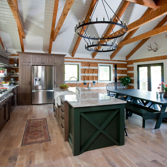 Sideview of kitchen with wood beams on ceiling, wooden floors, a green picnic style dining table, center island with green cabinets, and a white quartz countertop on island.