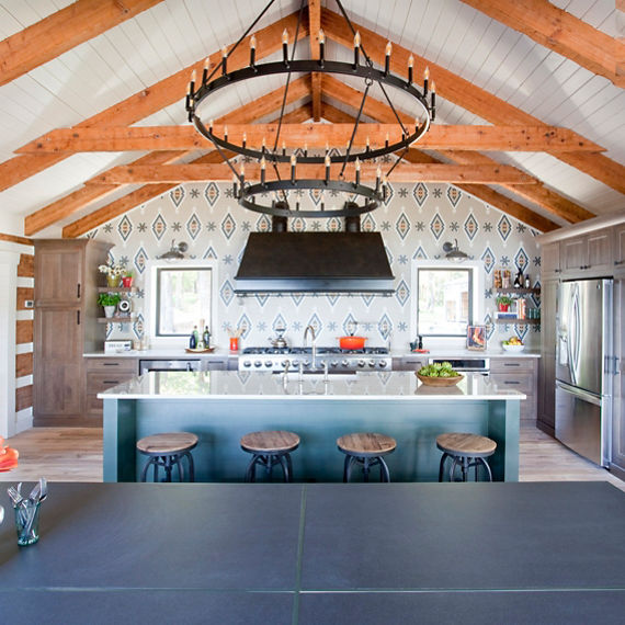 Kitchen with mosaic backsplash in diamond and flower pattern using beige hexagon mosaic tile, blue hexagon mosaic tile, orange mosaic tile, wood beams on ceiling, and white quartz countertops on counter and island.