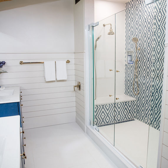 Bathroom with blue cabinets on sink, white porcelain countertops, and diamond pattern on shower walls using white hexagon mosaic tile and blue hexagon mosaic tile.