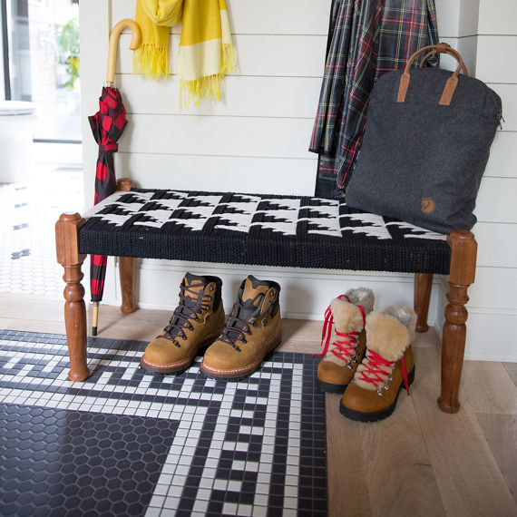 Mudroom with white hexagon mosaic tile and black hexagon mosaic tile on floor in pattern, two pairs of boots, sitting bench, and bag on sitting bench.