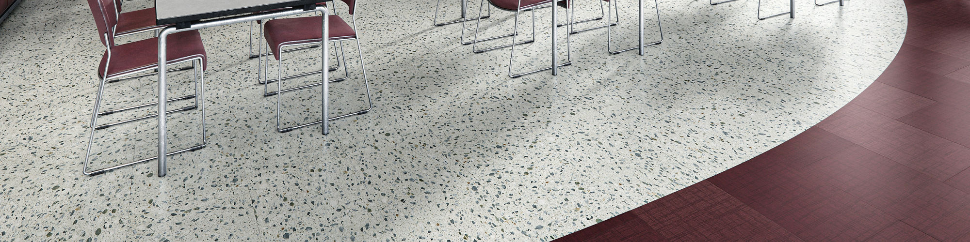 Cafeteria with white terrazzo look square floor tile, dark red fabric look rectangle floor tile, white tables, and red chairs.