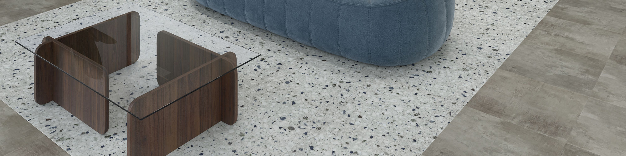 A contemporary office lounge features a plush blue sofa and two wooden side tables on a terrazzo rug. T