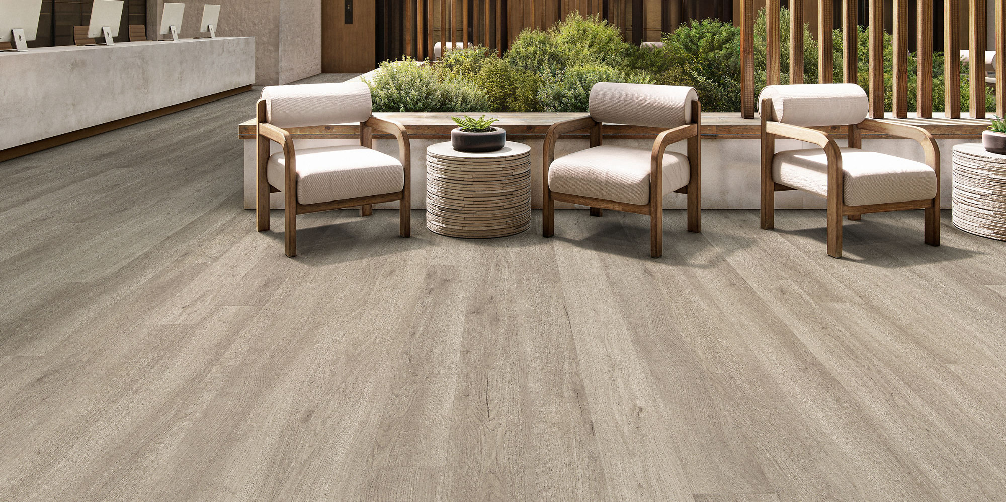 A spacious, contemporary hotel lobby features a central seating area with cushioned chairs and a round table. The setting includes natural wood accents, vertical slats, and indoor greenery, creating a welcoming and stylish atmosphere. The reception d