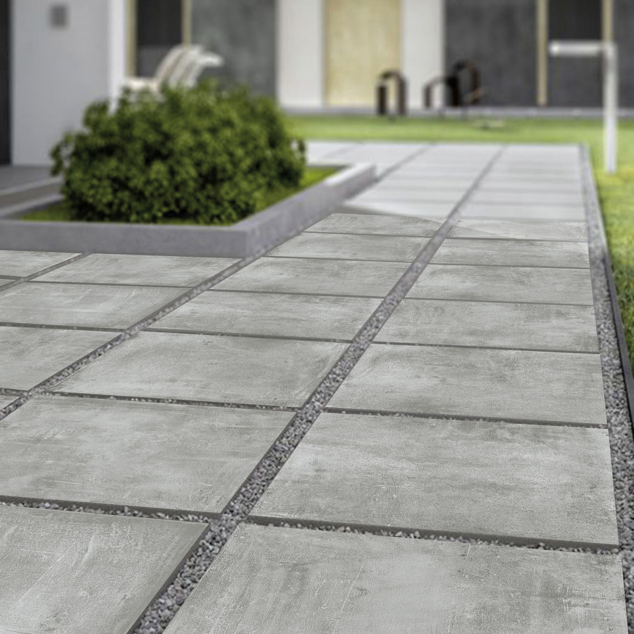 Closeup view of a walk with covered in concrete inspired porcelain pavers with gravel between the tiles and some green shrubs in the background.