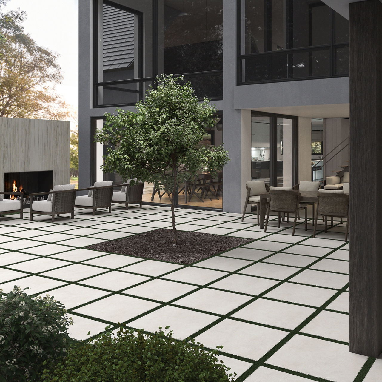 Large courtyard with a light, concrete inspired paver installed with turf on the edges surrounding a modular two-story home with a fireplace in the background.