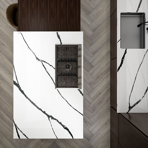 Overhead view of kitchen with white marble look quartz slab island, countertops, and backsplash. Light wood floors, wood dining table, and wooden chairs on side of island.