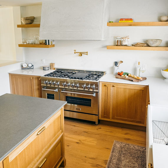 Kitchen with white marble look quartz countertop, wooden shelves and cabinets, and a gray concrete look quartz countertop on the center island..