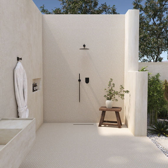 Outdoor shower with white penny round mosaic on walls and floor, small wood bench with plant, and trees in background.