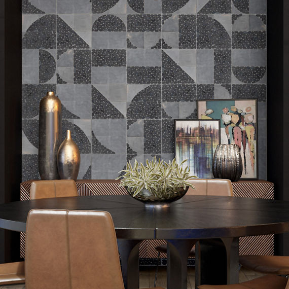 Dining room with gray pebble look mosaic on back wall, black round dining table, leather chairs, and art against the wall.