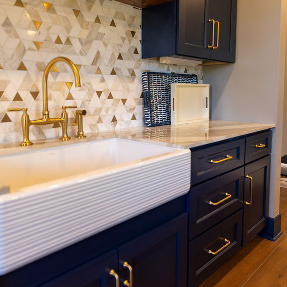 A contemporary kitchen features deep blue cabinetry with gold handles and a white farmhouse sink. 