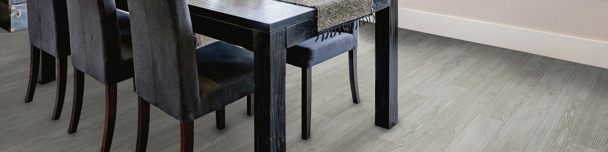Contemporary dining room featuring a dark wooden table and six upholstered chairs. Large picture windows surround the space, showcasing lush green trees and natural light. A rectangular glass pendant light hangs above the table, complementing the neu