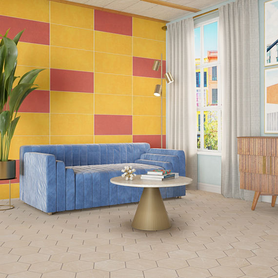 Living room with feature wall of bright yellow and red tile, blue velvet sofa, beige hexagon marble look floor tile, and small round coffee table with brass base.