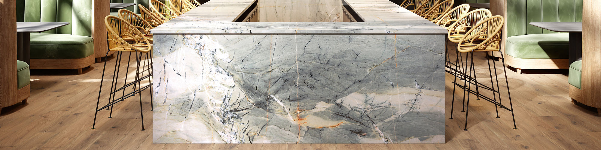 Restaurant with light blue quartzite slab bar in center, green booths on the side, wicker bar chairs, and wood look tile on floor.