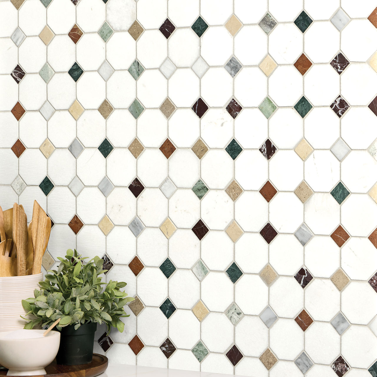 A decorative kitchen backsplash features a repeating pattern of white hexagon tiles with small diamond-shaped insets in various earthy colors. The tiles include brown, green, beige, and gray accents that create a subtle geometric mosaic. In the foreg