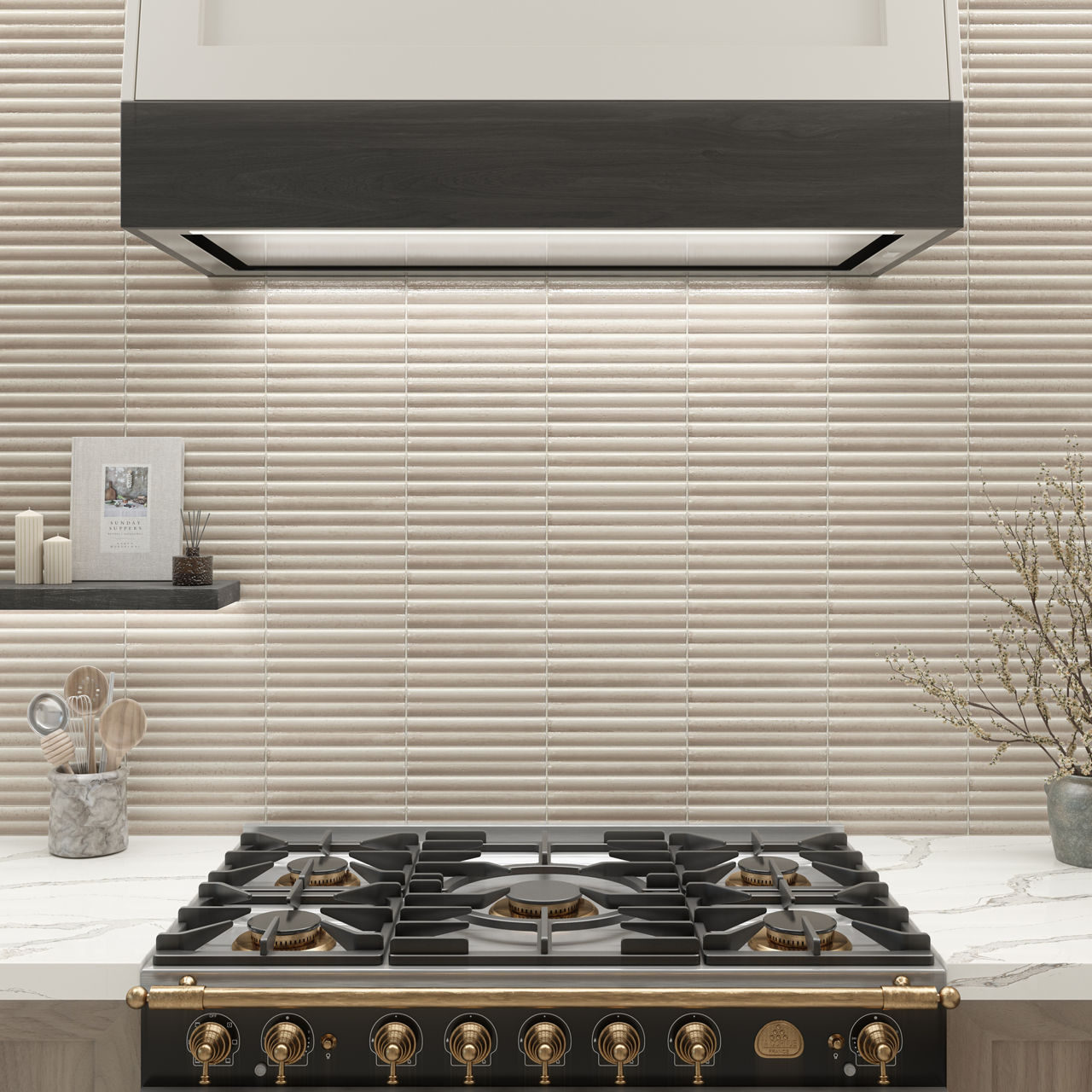 A modern kitchen with warm beige fluted 2x10 tile backsplash, black and gold gas range beneath a sleek hood, marble countertop, and neatly arranged utensils.