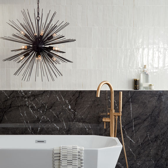 Bathroom with white subway tile on top half of wall, black quartz on bottom half of wall, white tub, and gold accents.