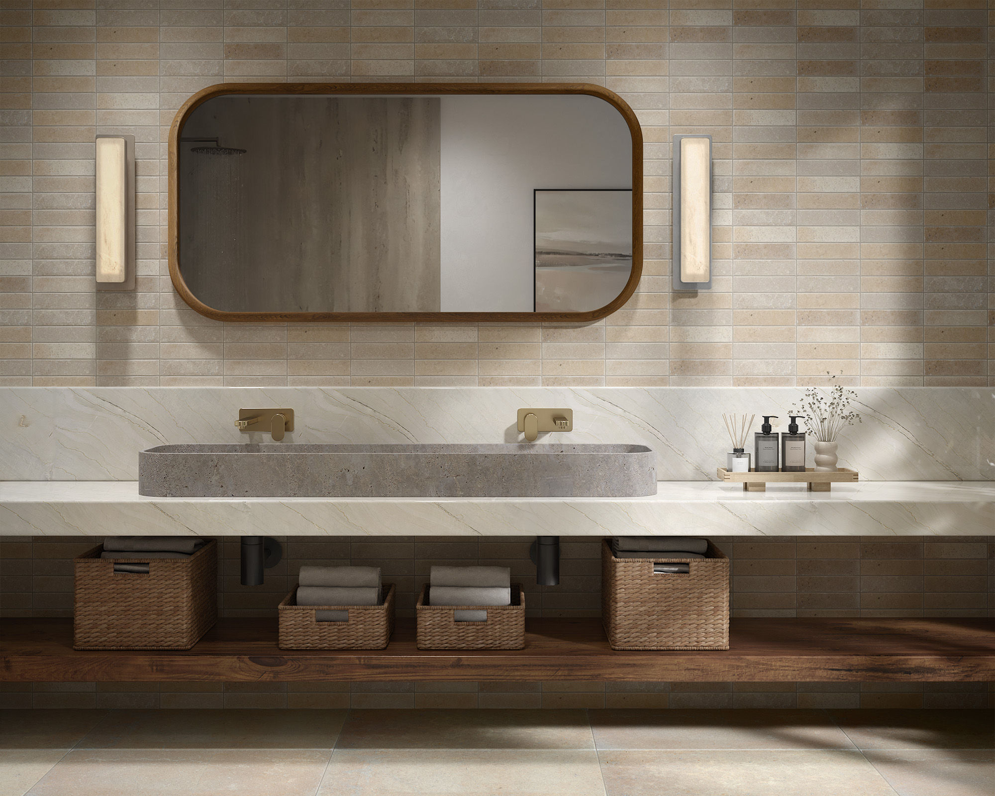 A contemporary bathroom features a long stone double sink set into a sleek floating countertop. The wall behind the vanity is covered in warm neutral tiles, complemented by an oval mirror and two vertical wall sconces. Woven storage baskets with towe