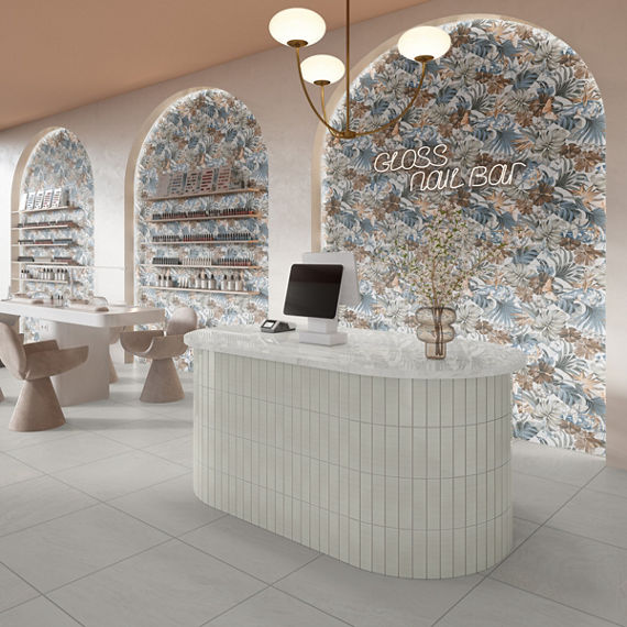 Nail salon with white subway tile on welcome desk, white concrete look square floor tile, arched wall niches, and white nail table with beige chairs.