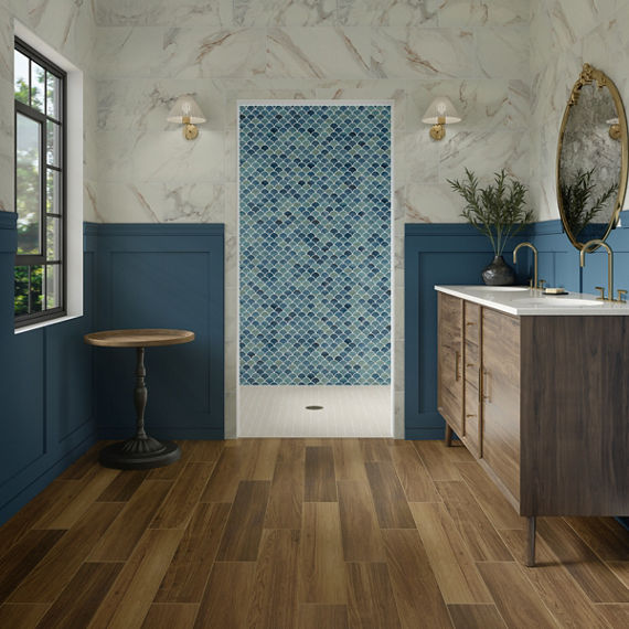 Bathroom with wood look floor tile, wood cabinets, white countertop, white marble look tile on top half of wall, and blue arabesque tile on back wall.