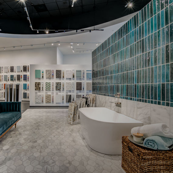 Showroom bathroom vignette featuring a freestanding bathtub, teal wall tiles, and surrounding tile sample displays.