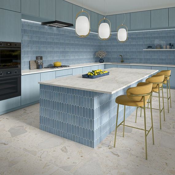 Kitchen with center island, yellow bar chairs, blue fishscale walls and backsplash, and a white stone look floor tile.