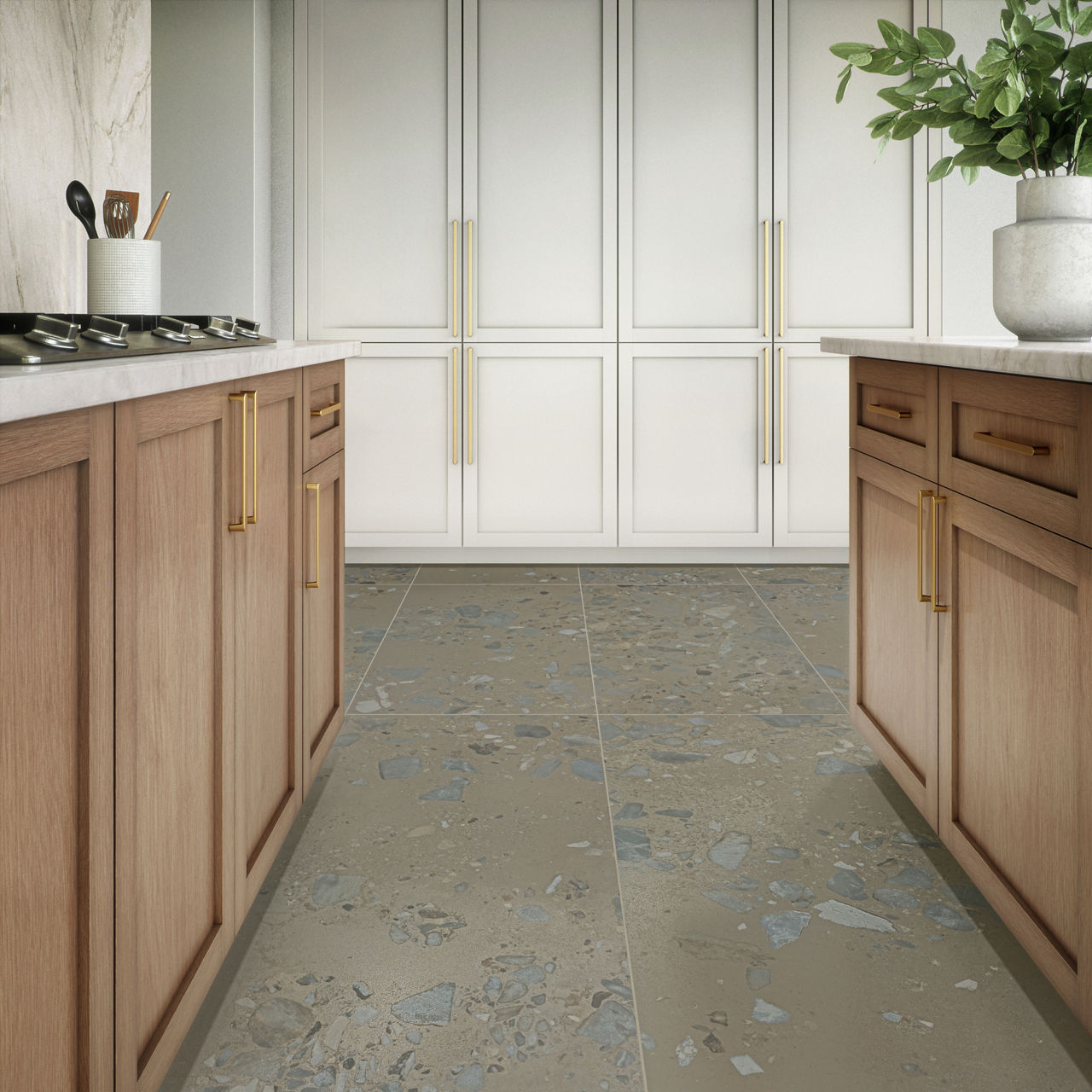 A contemporary kitchen features a corridor layout with wooden base cabinets on both sides. Light wood cabinetry with gold handles contrasts with tall white cabinets at the far end. The floor is covered in large terrazzo-style tiles with scattered sto