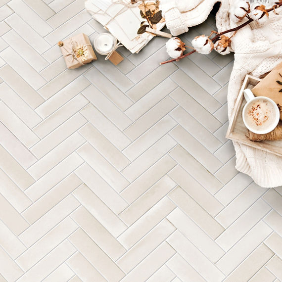 Closeup birds eye view of beige herringbone floor tile that looks like concrete, off white sweater, latte in mug, stems of cotton bolls and candle wrapped in twine.