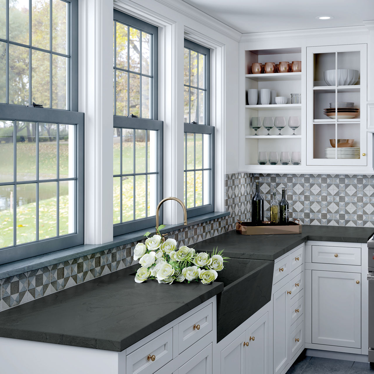 Kitchen with windows over kitchen sink, white cabinets, and gray and blue geometric patterned square tile on the backsplash.