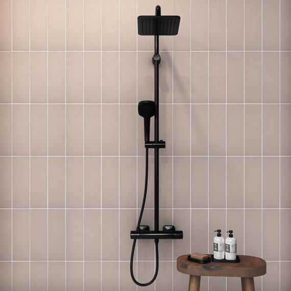Shower with pink linear rectangle tile in a vertical pattern, a black showerhead, and a small wooden shower table with shampoo and conditioner.