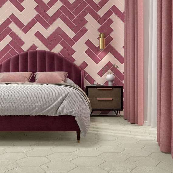 Art deco style bedroom with pink tile on back wall, white hexagon floor tile, a pink bed with pink headboard, a wooden nightstand, and pink and white curtains.
