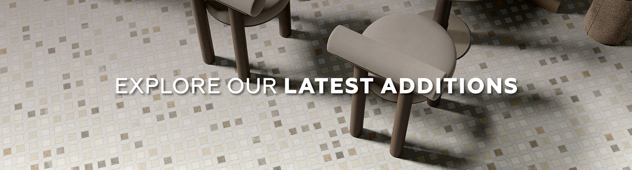A top-down view shows a modern tiled floor with a subtle geometric pattern of small square tiles. Two contemporary chairs are partially visible, suggesting a stylish interior setting. Bold white text across the center reads "EXPLORE OUR LATEST ADDITI