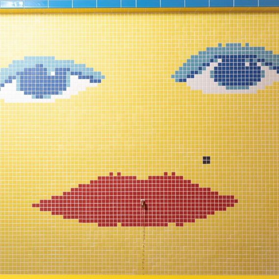 Wall fountain with yellow, blue, white, and red mosaic wall tile that looks like a face.