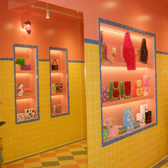 Susan Alexandra accessory store with purses in shelves on bright yellow wall tile with bright blue trim, yellow, blue, green, and orange checkerboard floor tile.