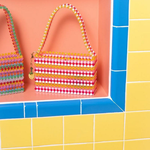 Susan Alexandra yellow, white, light pink and bright pink beaded purse on wall niche surrounded by bright blue bullnose tile and bright yellow wall tile.
