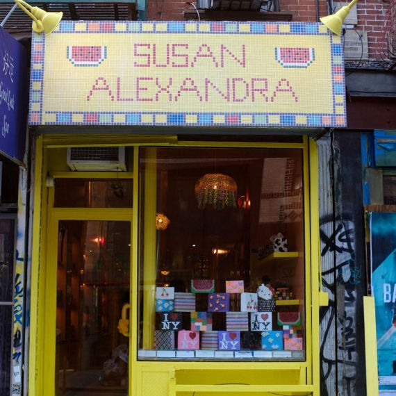 Storefront with neon yellow door and window frame, Susan Alexandra sign made of yellow, red, and blue mosaic tile over the door and window.