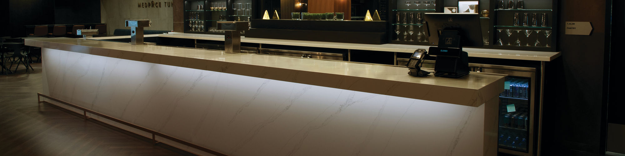 FC Cincinnati TQL Stadium tunnel club bar with base and countertops made of marble look white quartz with gray veining, and shelves holding cocktail glasses.